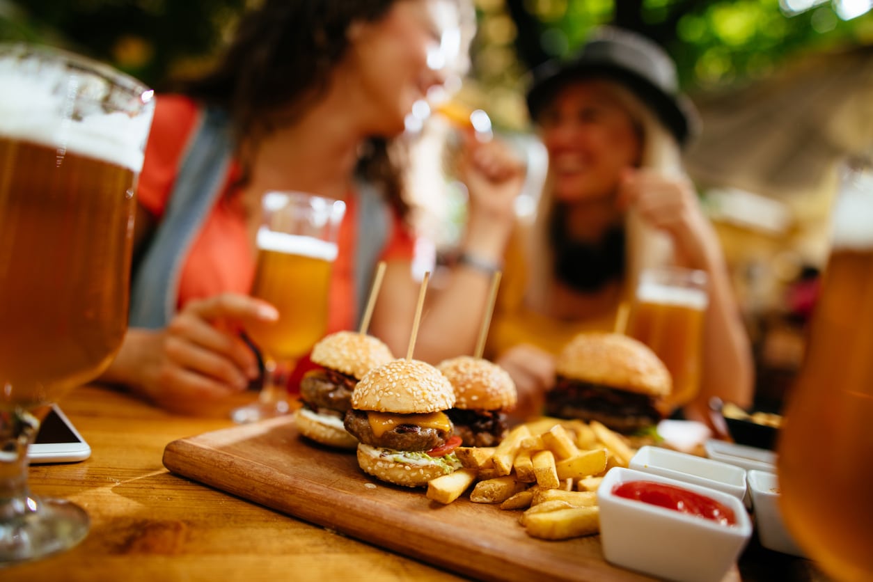 Summer outdoor dining - A group of friends enjoying mini cheeseburgers and fries with their glasses of beer.